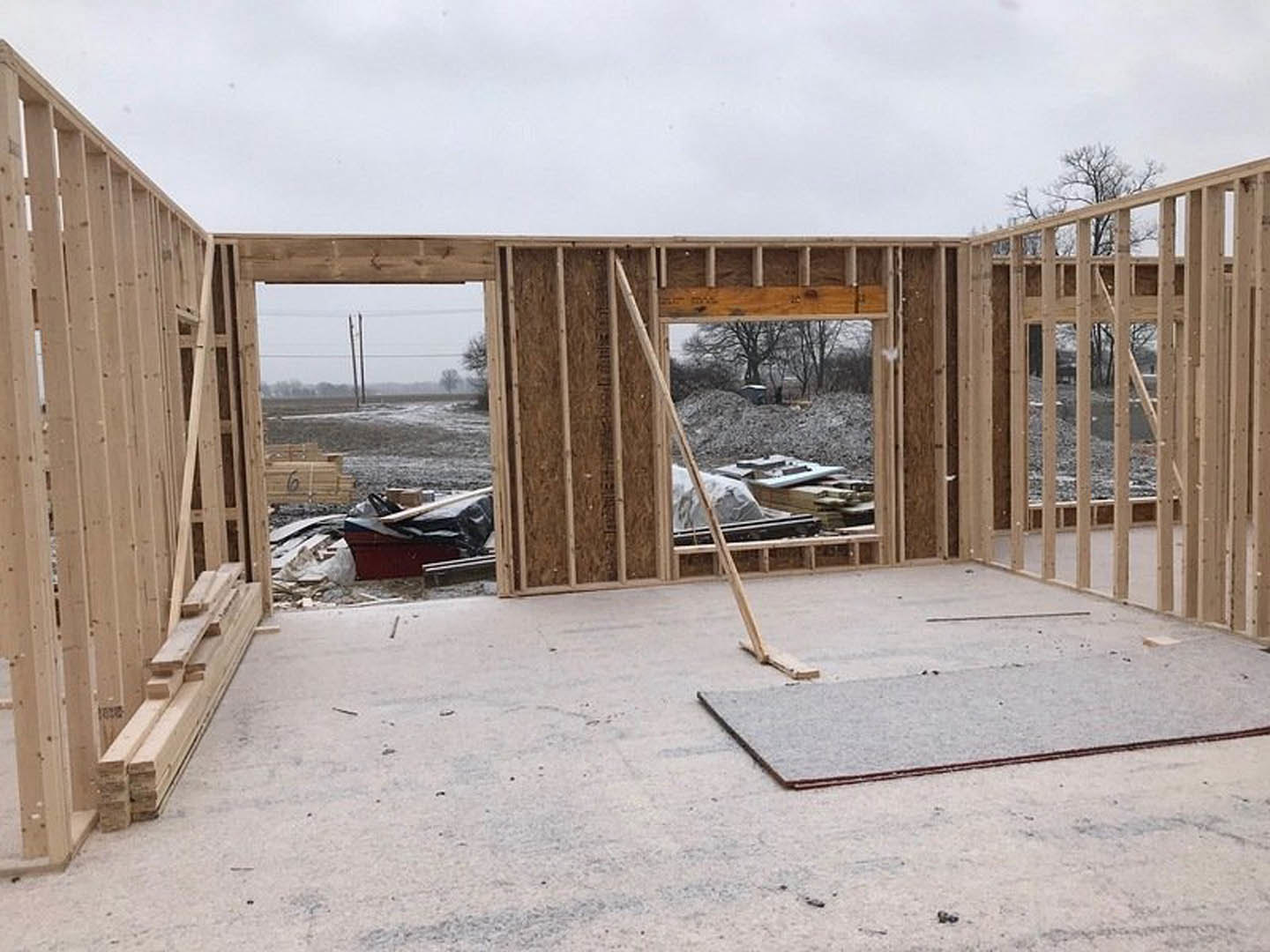 Unfinished room with exposed wooden framing, concrete floor, large window, and snow-covered ground outside