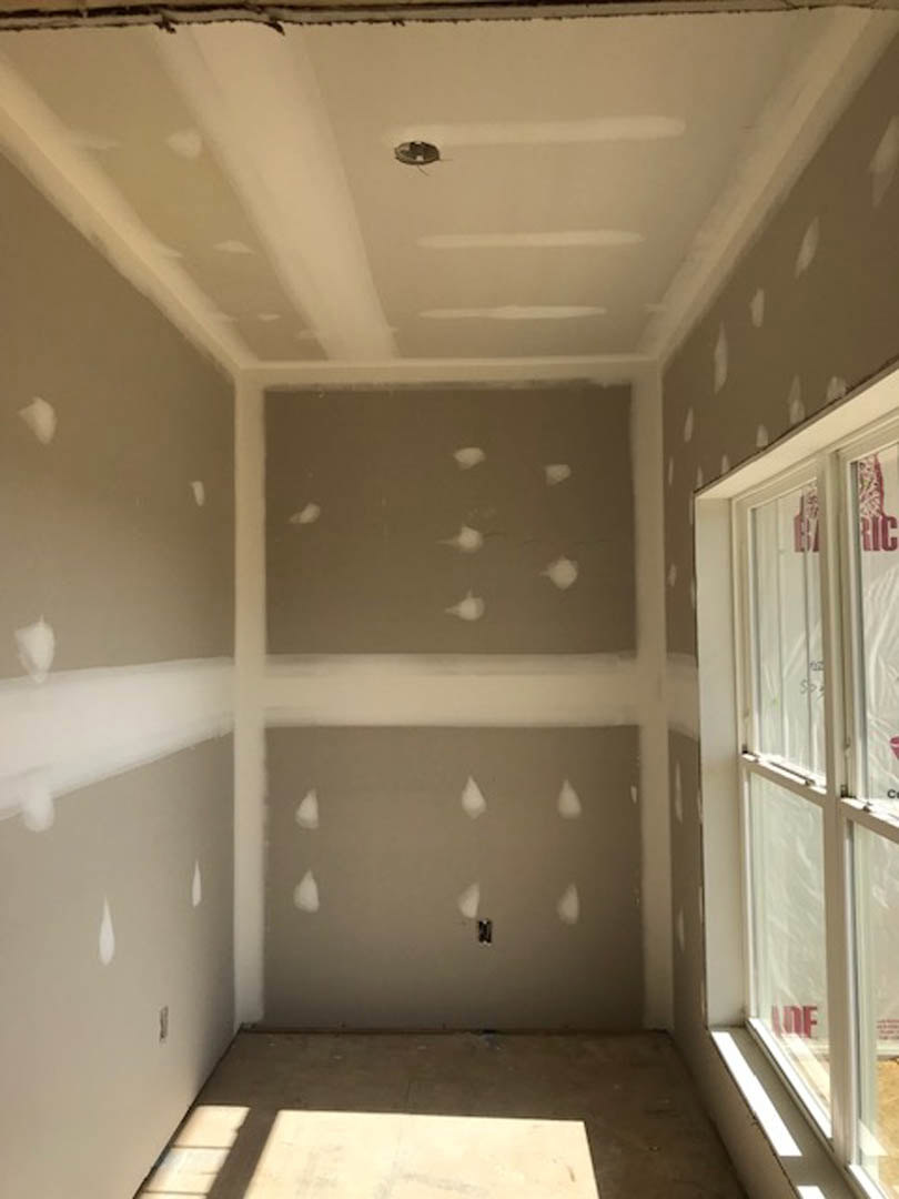 White-painted walls with black-bordered window, recessed ceiling lights, and grey floor featuring scattered white dots