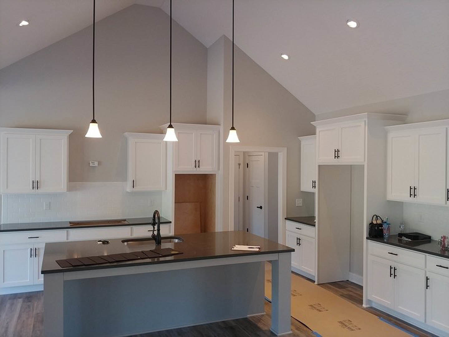White shaker cabinets with matte black countertops, stainless steel sink, white tile backsplash, and pendant light with white shade