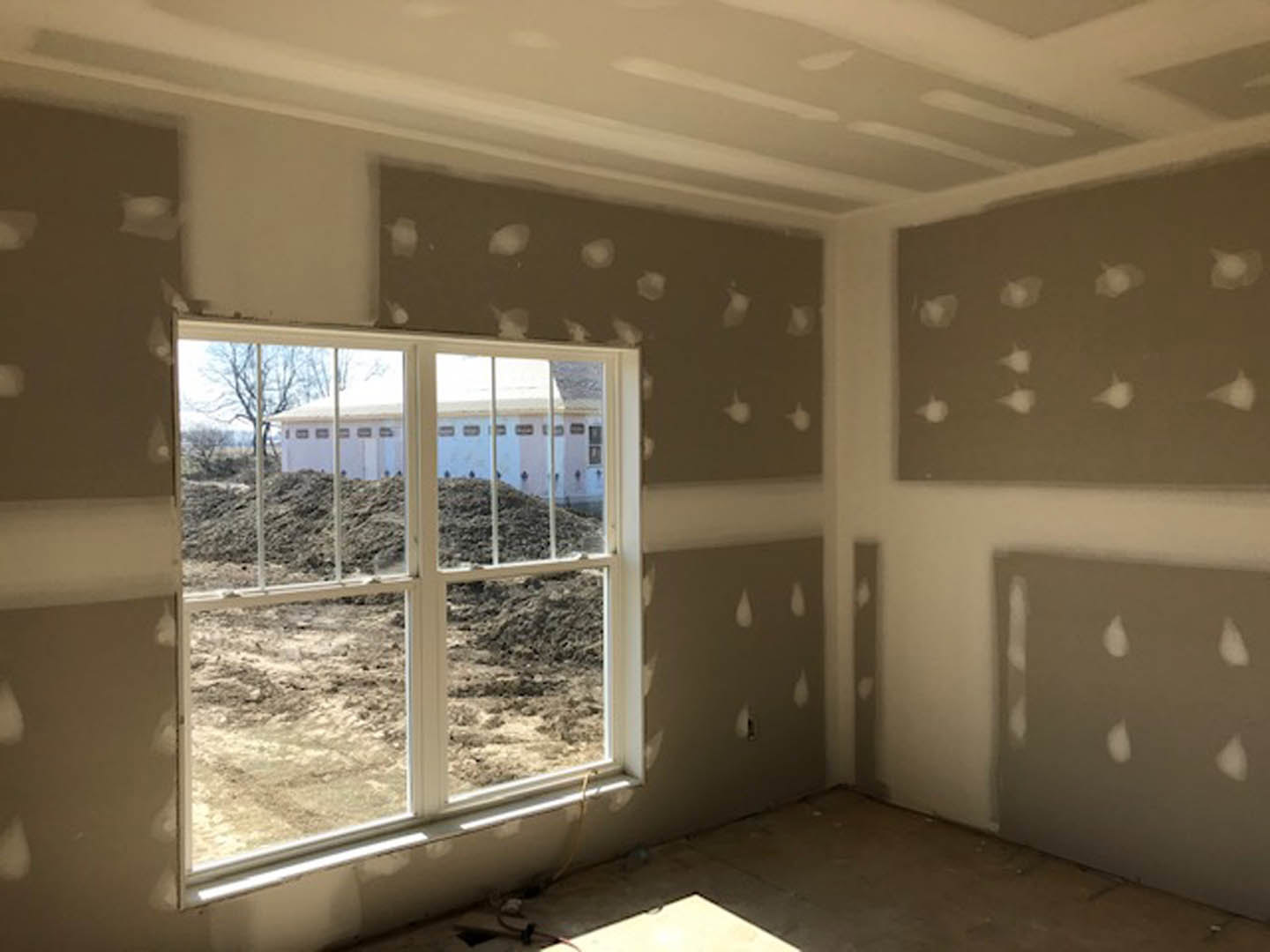 Sunlit room with plaster walls, large window overlooking a blue building, tile floor, and ceiling with recessed lighting.