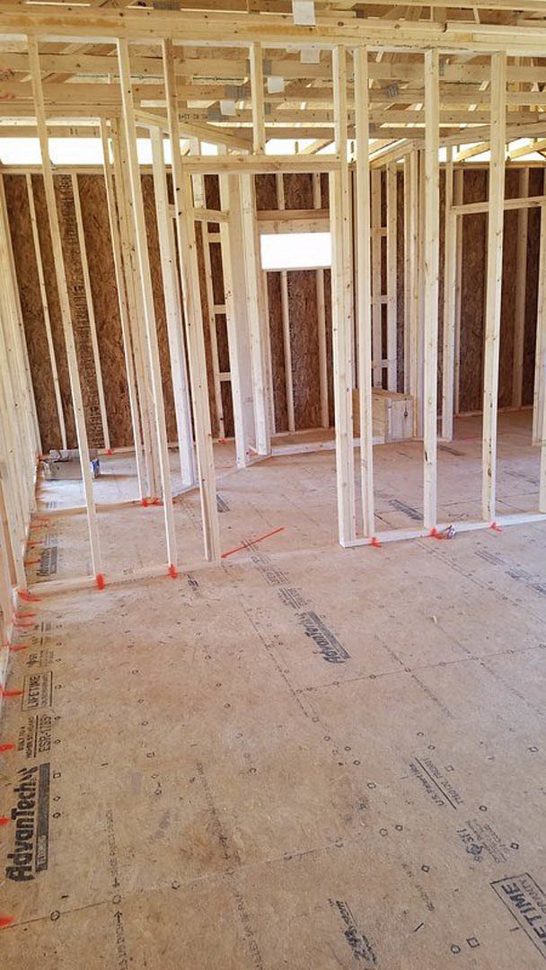 Exposed wood framing and beams in a partially constructed room with unfinished floor and building insulation visible