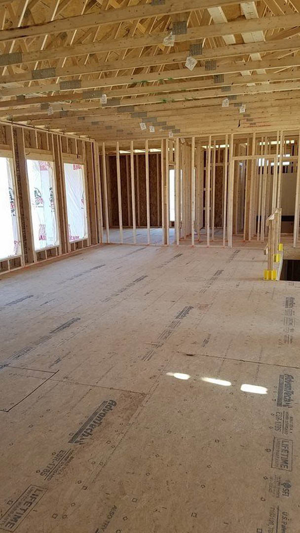Spacious room under construction with exposed wood framing, ceiling beams, unfinished floor, and several windows letting in natural light