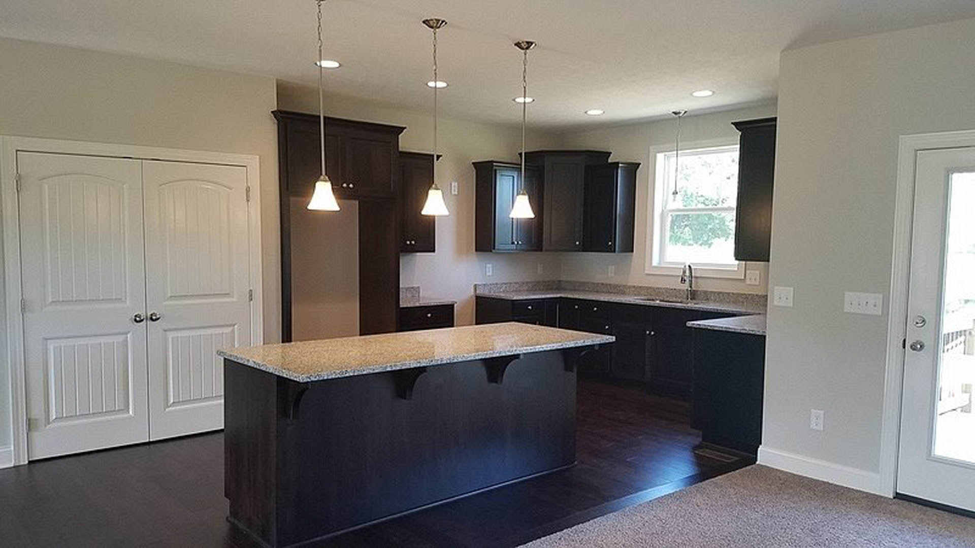 Kitchen with dark wood cabinets, light stone countertop, tile backsplash, stainless steel sink, and neutral flooring