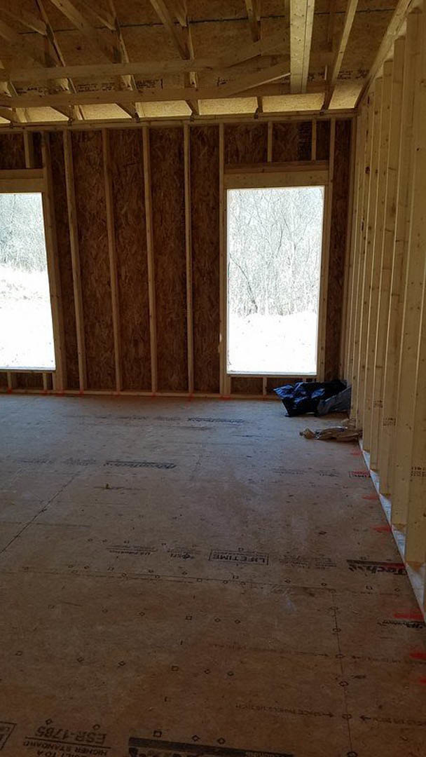 Wood-beamed ceiling and plank floor in a room with two windows overlooking snowy trees, wooden door on one wall