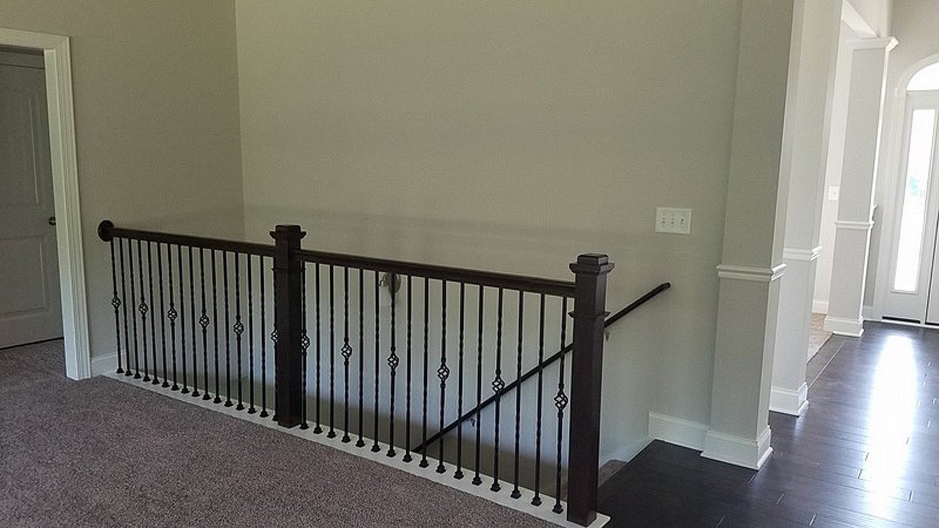 Black iron railing staircase with light wood steps, white walls, and a wall outlet with buttons visible near the base.