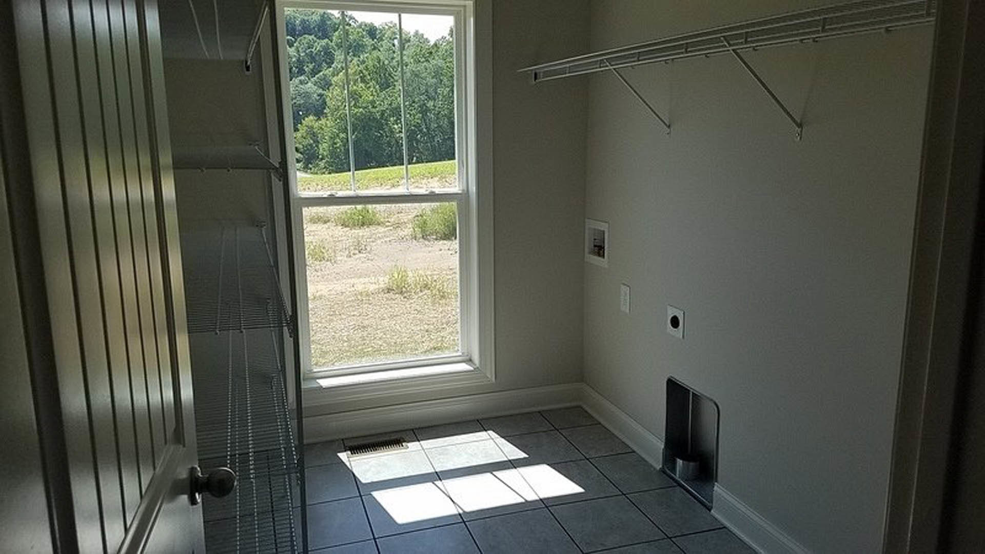 Bright interior room featuring a large window, built-in wall shelf, light tile flooring, and white walls.