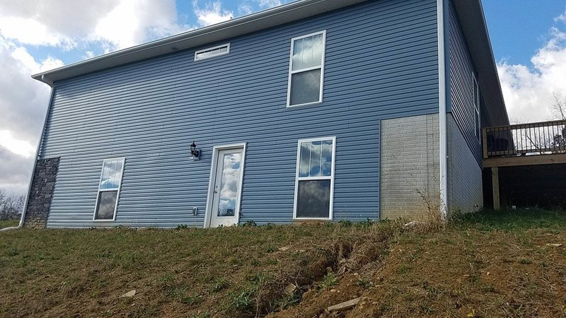 Blue siding exterior with white front door, multiple windows, green lawn, and partly cloudy sky