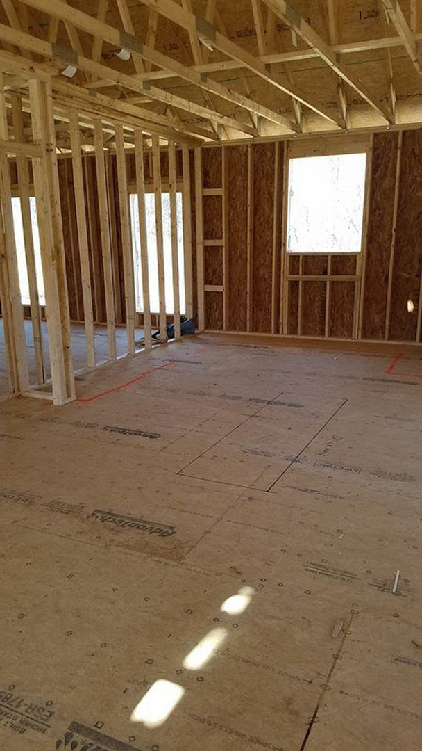 Room under construction with exposed wood framing, grid-style window letting in natural light, unfinished ceiling beams, and subfloor visible