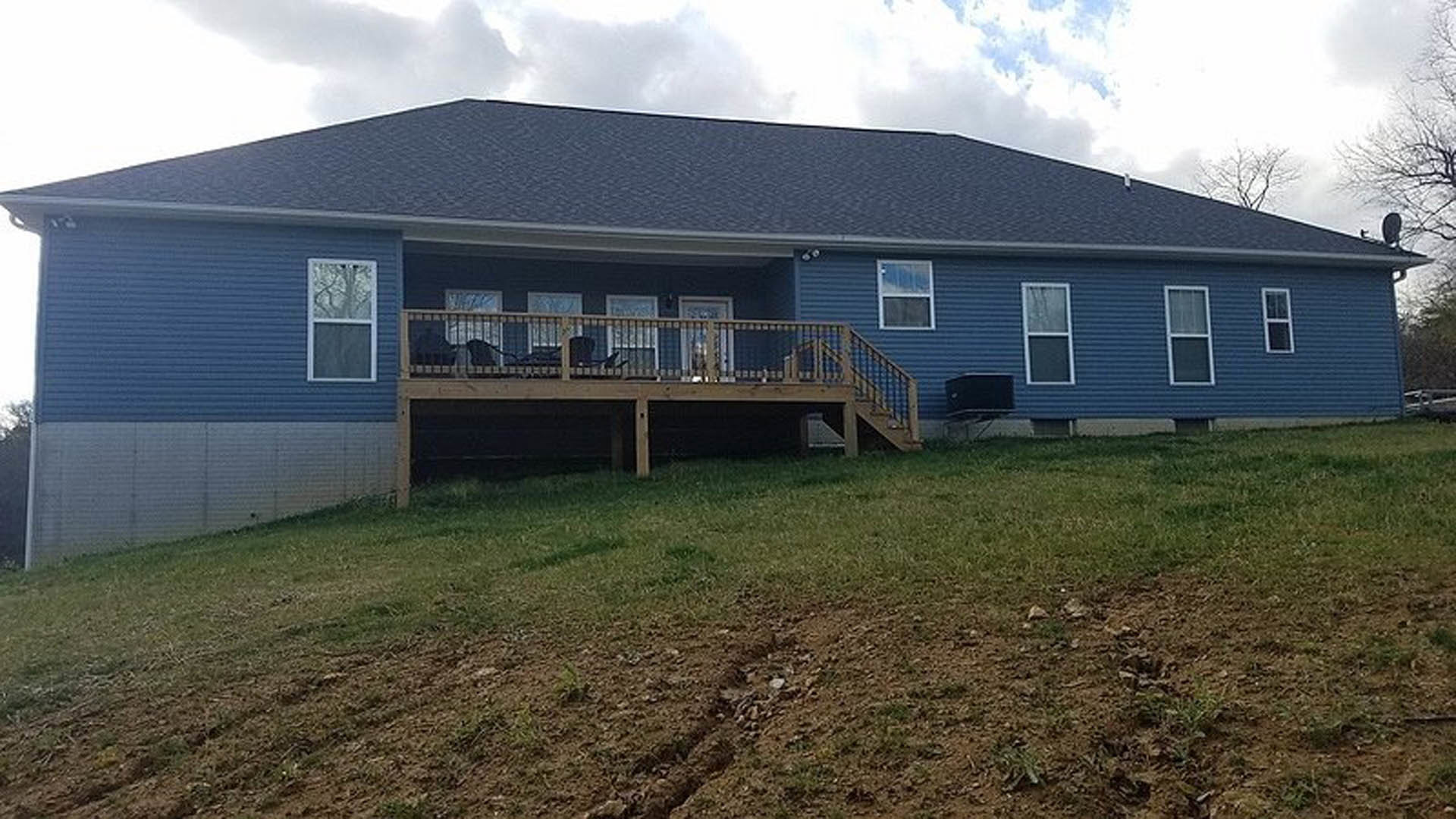 Two-story home with white siding, large windows, wooden deck furnished with a chair, and green lawn under partly cloudy sky