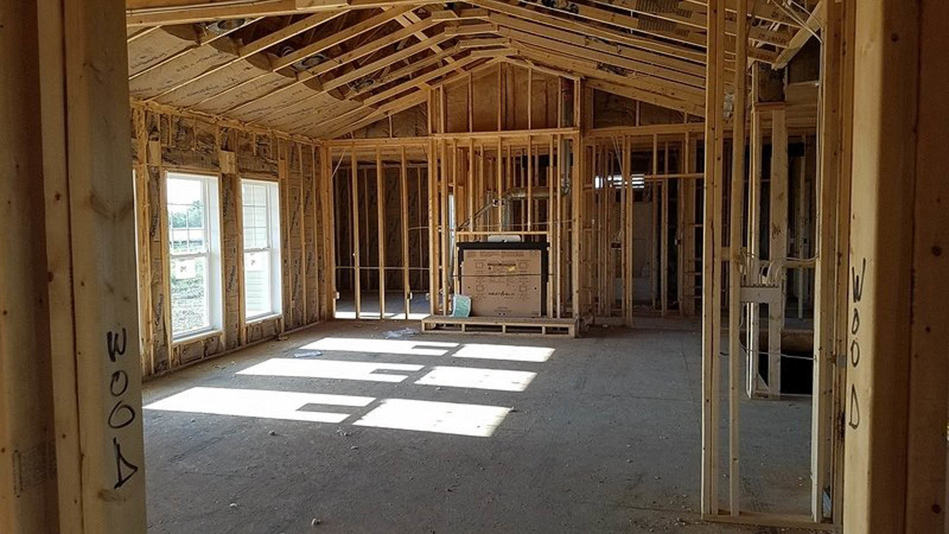 Spacious room featuring a large window with natural daylight, exposed wood beams, light-colored ceiling, and visible wooden plank flooring.