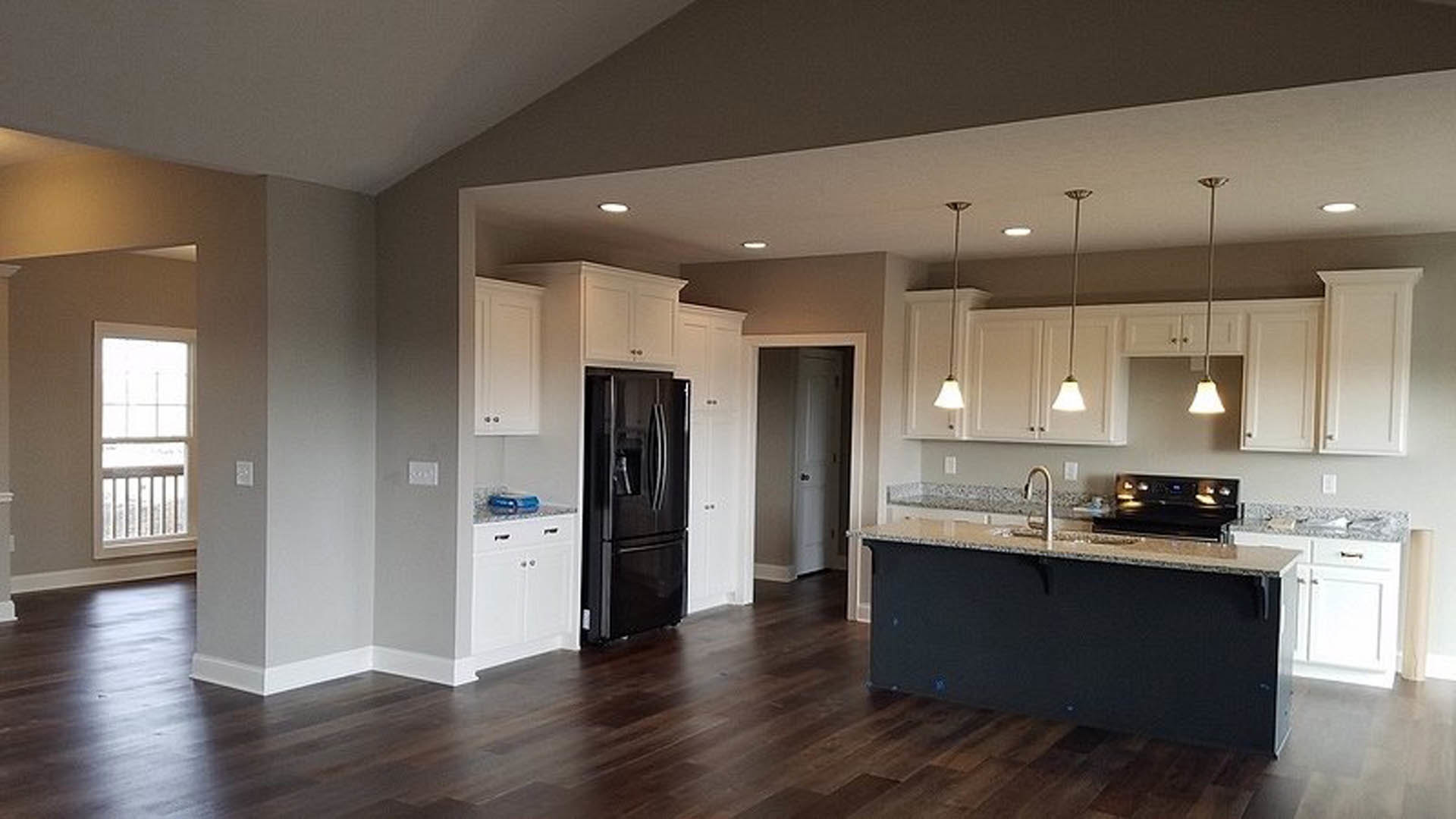 Modern kitchen featuring a matte black refrigerator, white cabinetry, stone countertops, stainless steel sink, and pendant lights with white shades hanging from the ceiling