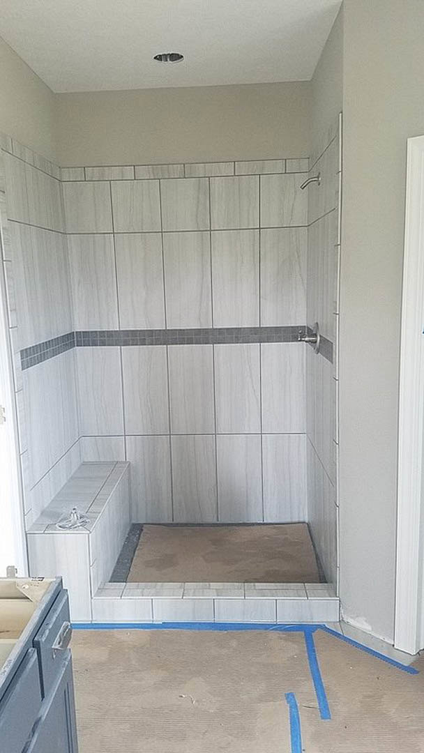 Walk-in shower with light grey tile floor, white plaster walls, and built-in cabinetry.