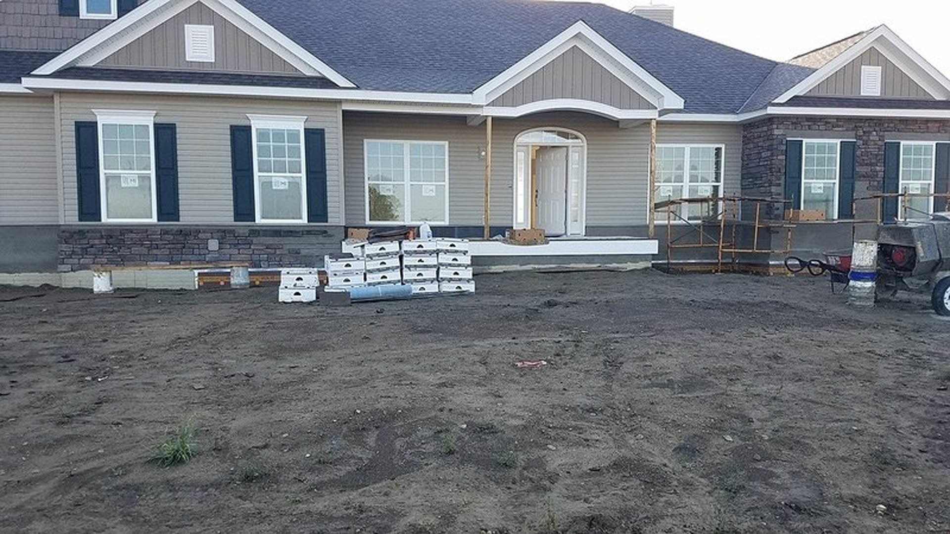Gray-sided house with white-framed windows, white vent, and a stack of wooden pallets on the porch.