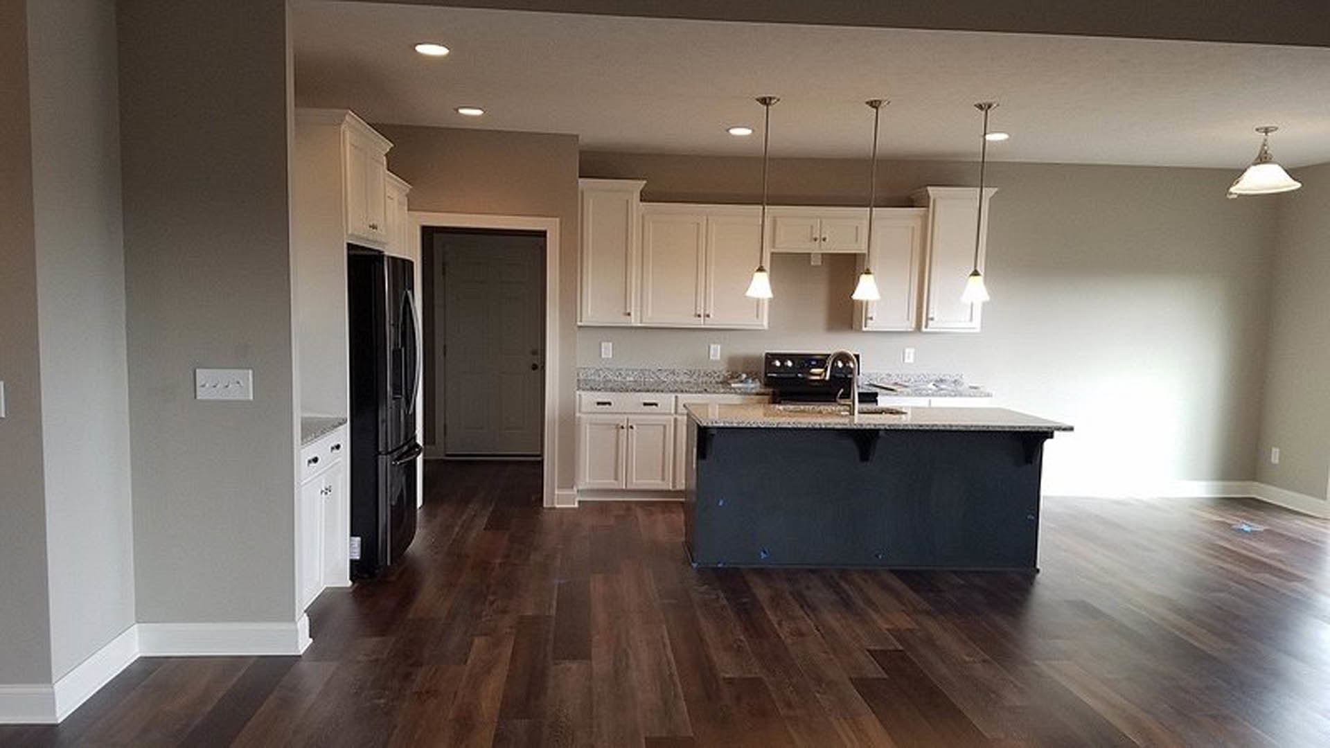 White kitchen cabinets, black island with matching countertop, tile backsplash, laminate flooring, recessed lighting, stainless steel sink