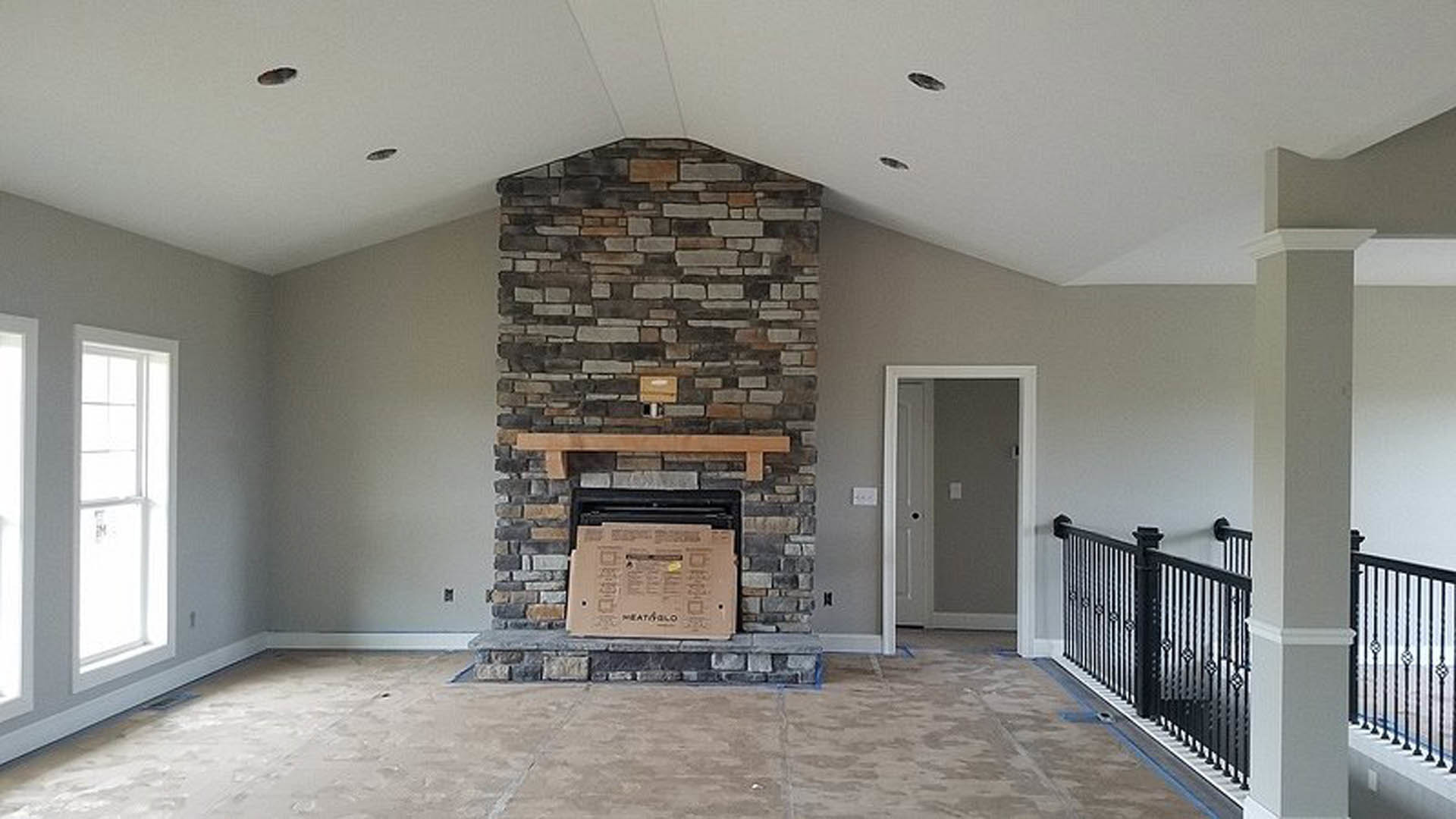 Stone fireplace with white plaster surround, wood mantel, light hardwood floors, and decorative wall molding in a spacious living room.
