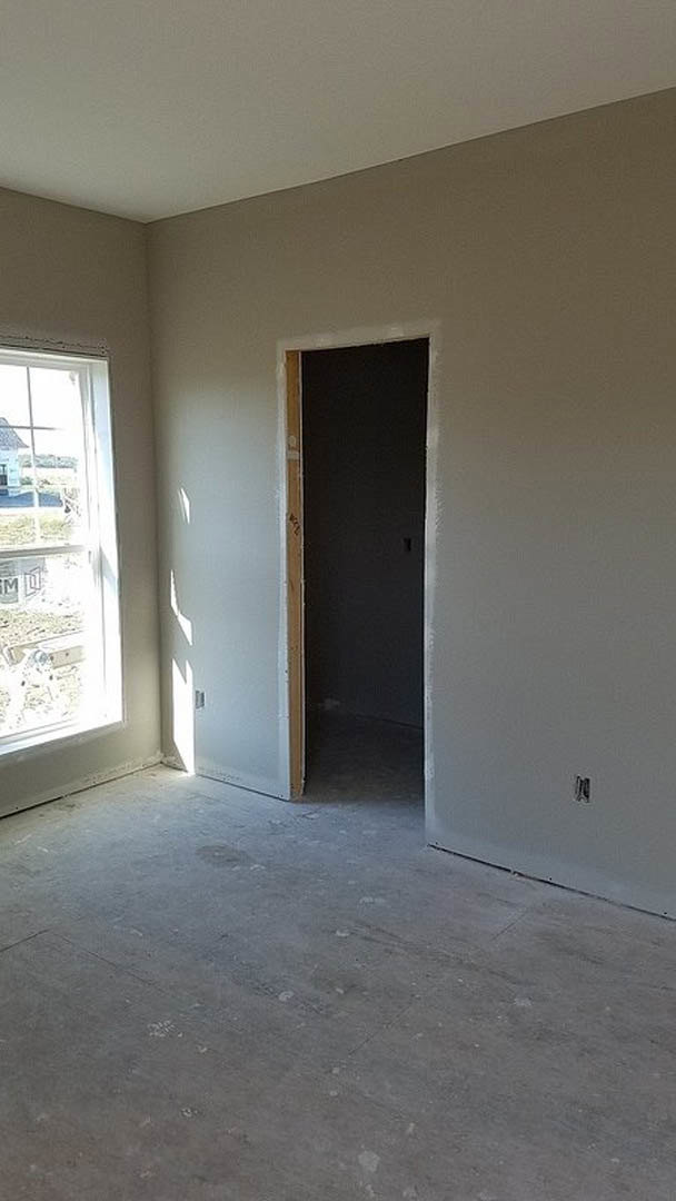 Black door with white frame open onto concrete floor, white-framed window on adjacent wall, smooth grey plaster surfaces throughout room.
