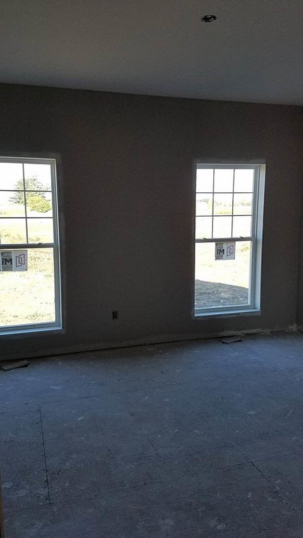 Room with two large windows, concrete floor, white walls, and a sign taped to one window