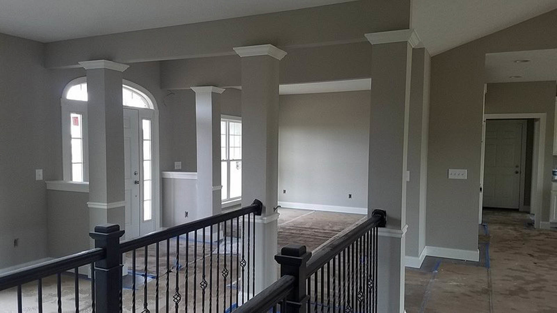 Entryway with white plaster columns, black metal railing along staircase, light wood flooring, and neutral walls