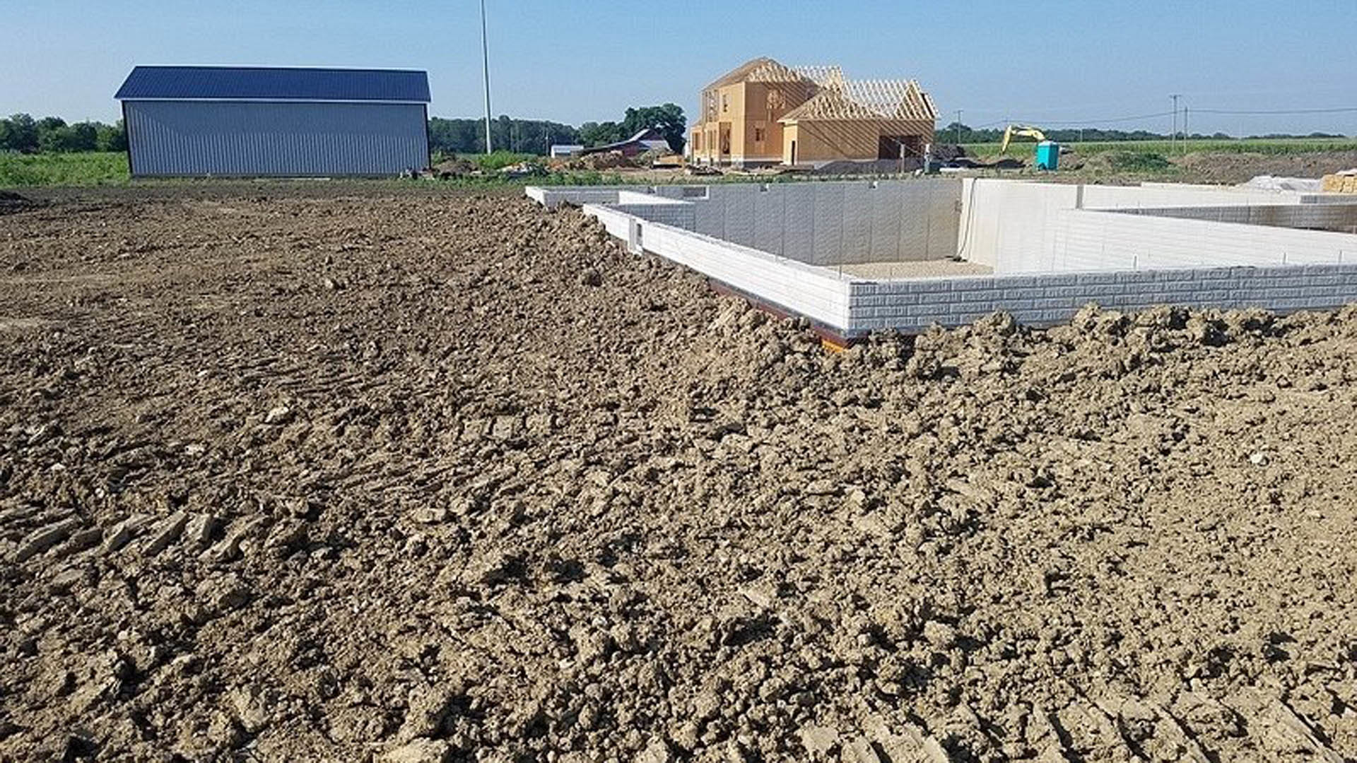 Concrete foundation slab on a residential building site surrounded by soil, construction materials, and open sky