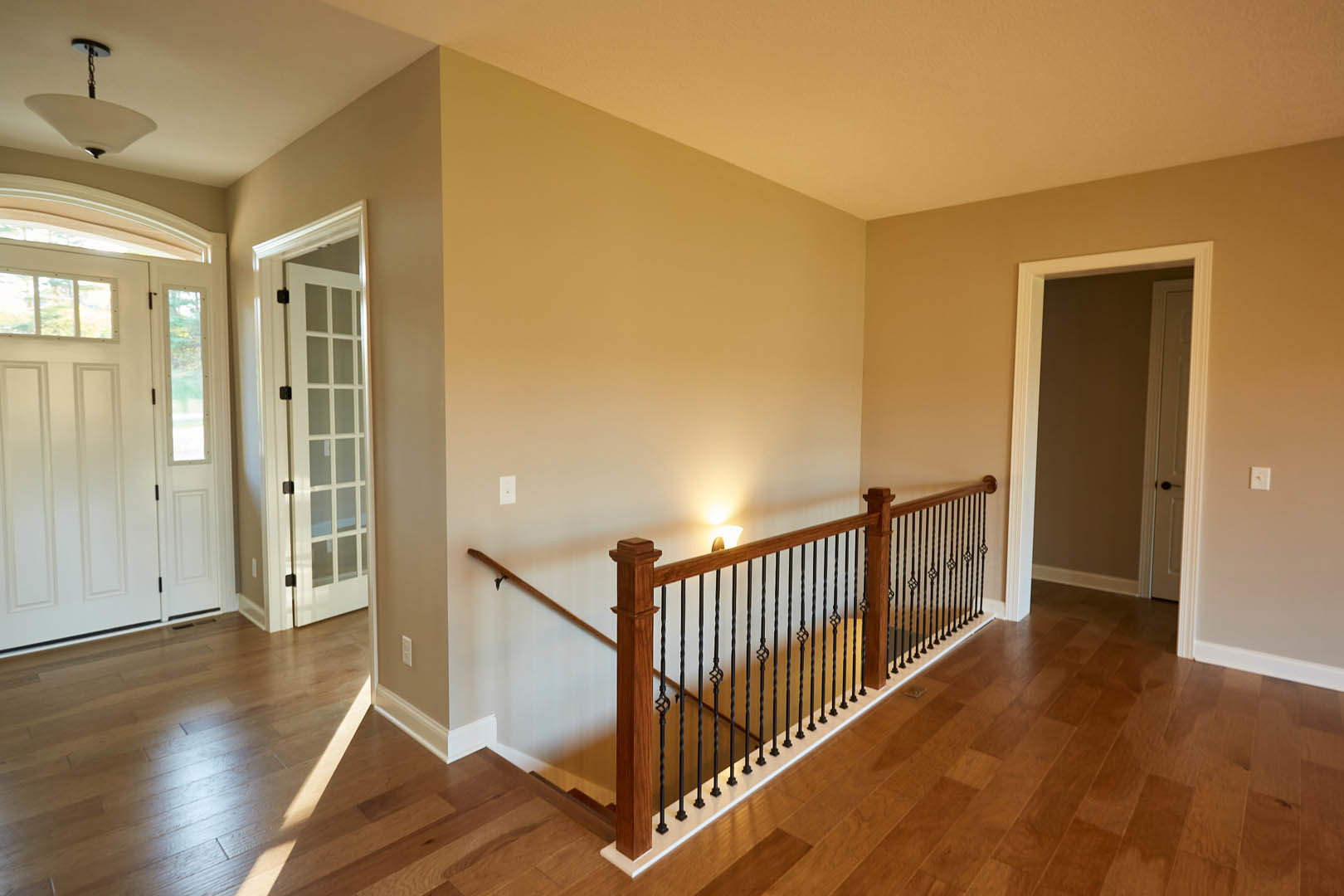 Wooden staircase with black metal railing, white door in doorway, hardwood flooring, and modern light fixture in residential interior.