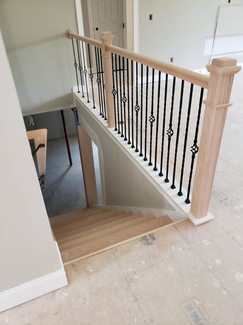 Wood staircase with matte black metal railings, light-colored walls, and hardwood flooring in a modern interior.