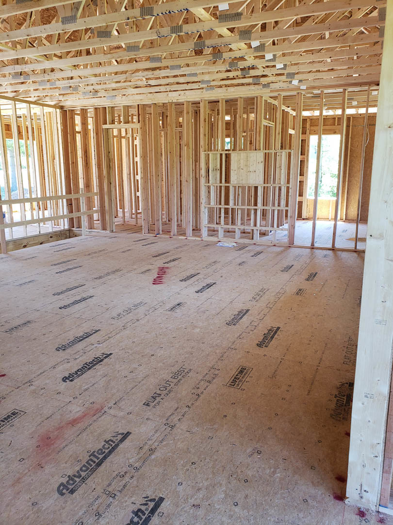 Wood-framed room under construction with exposed beams, unfinished floor, and open ceiling structure