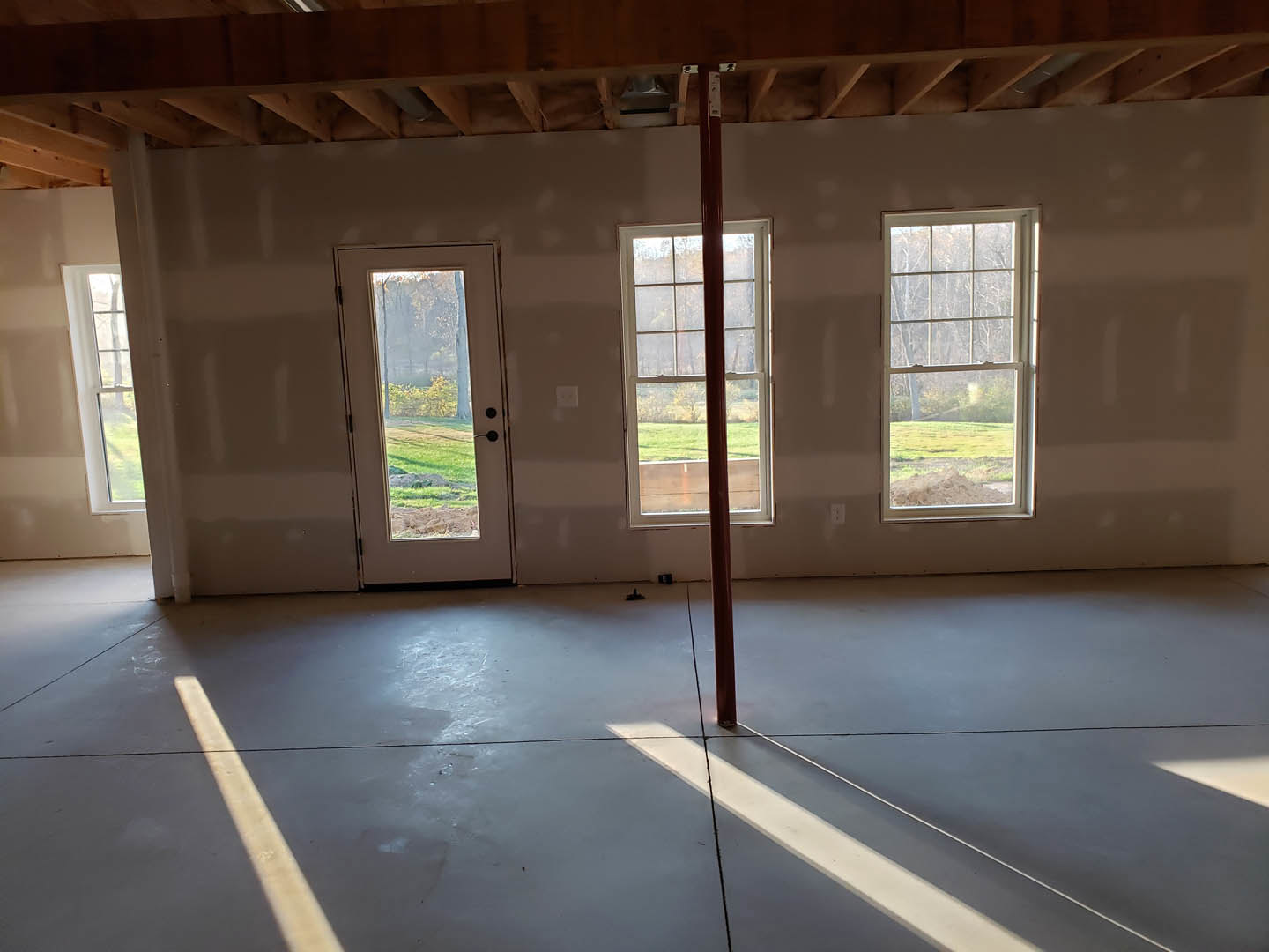 Spacious room with large windows, glass door opening to grassy yard, concrete floor with white line, and metal support pole near window.