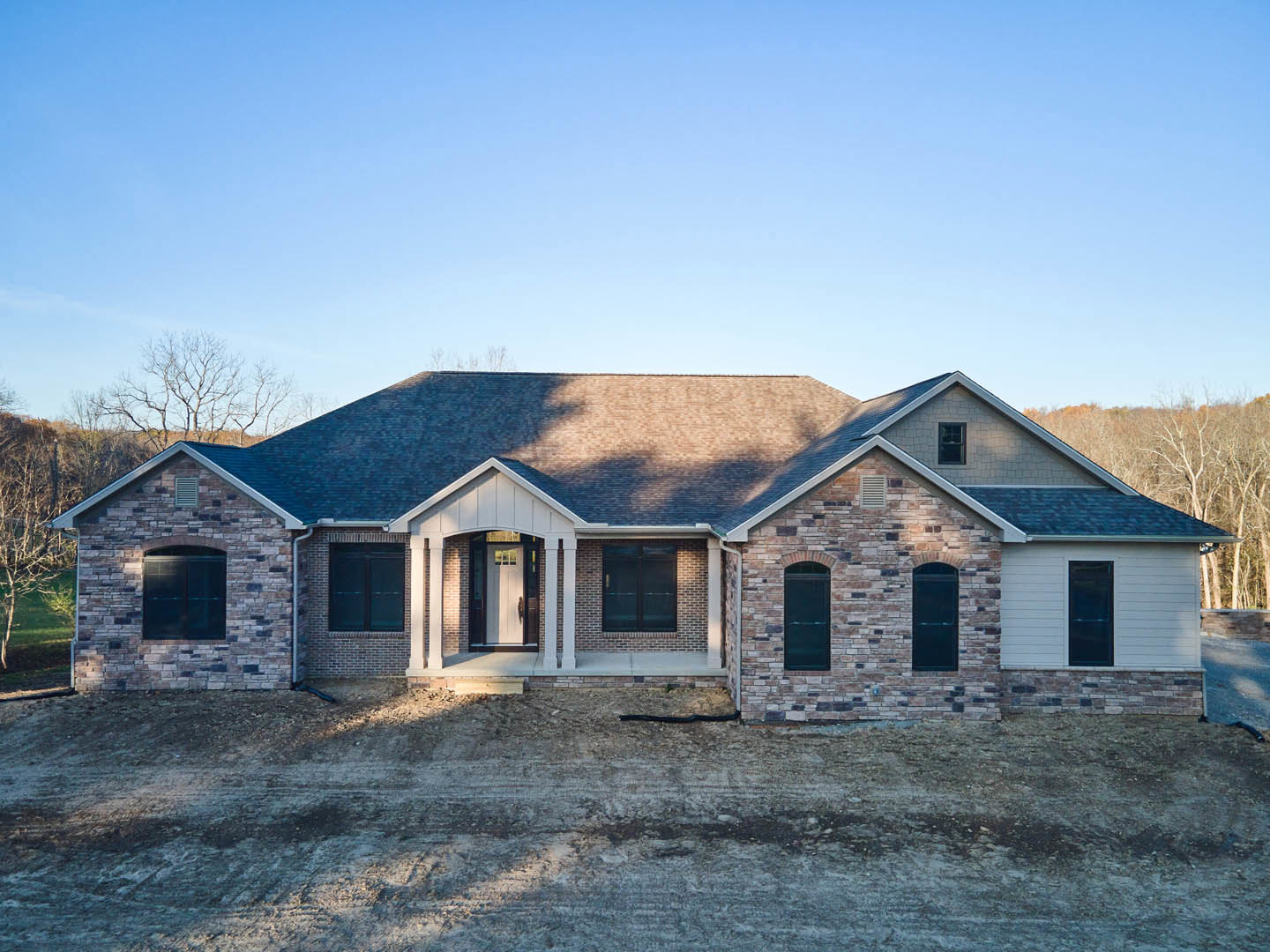Brick house with black-framed windows, covered porch, and unfinished dirt yard under a clear sky
