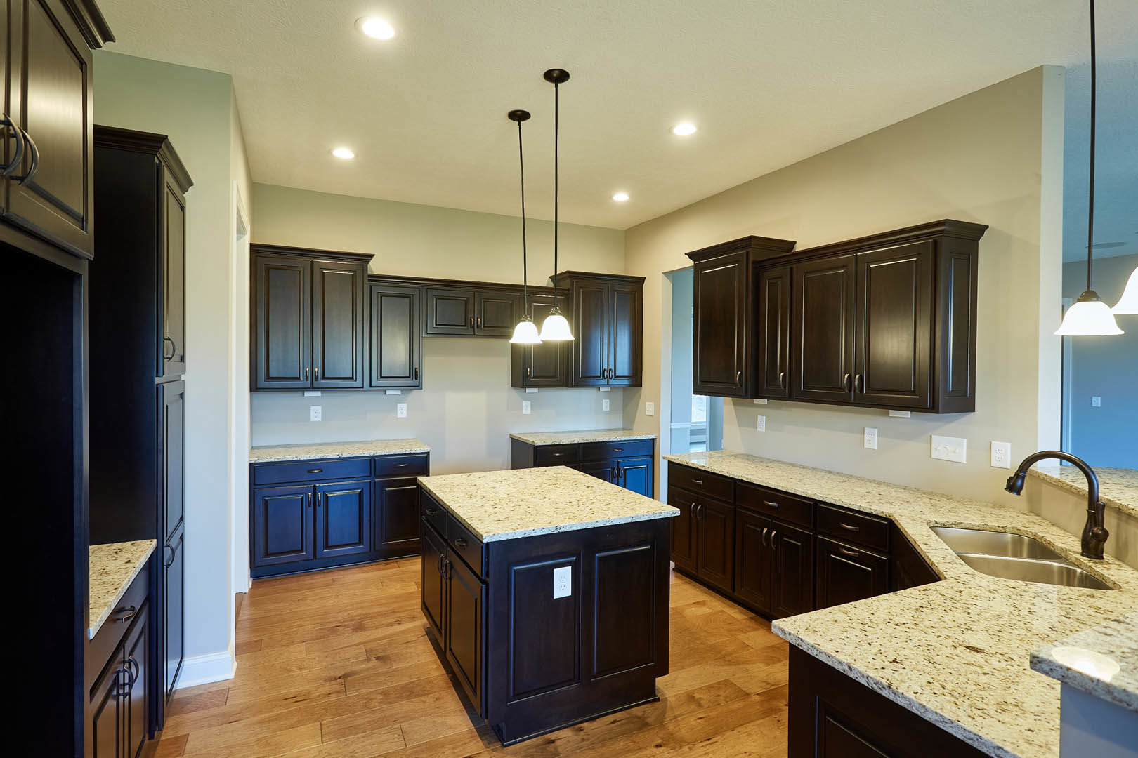 Kitchen with dark wood cabinets, granite countertops, central island with marble surface, stainless steel sink, and modern appliances