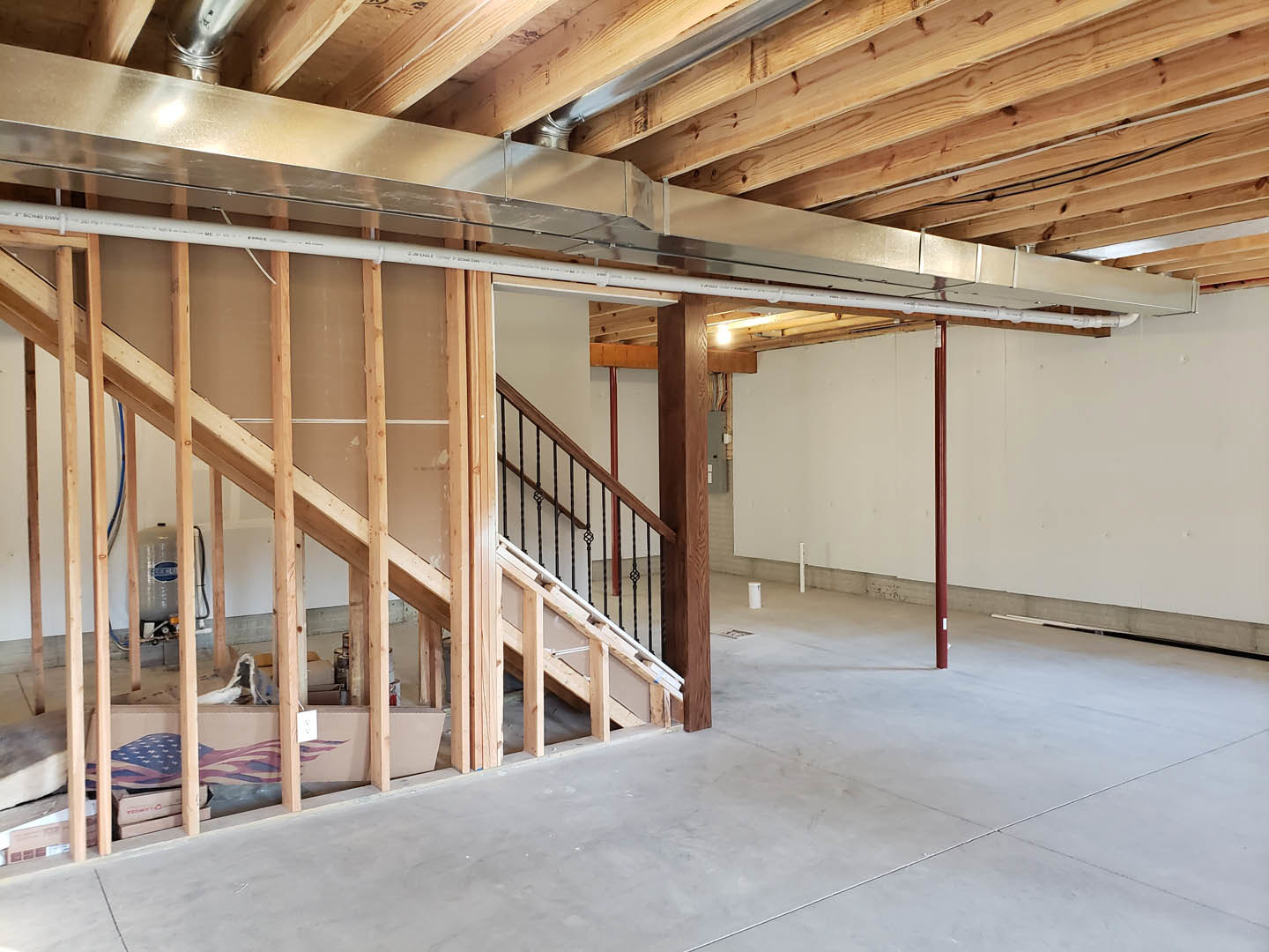 Staircase under construction with exposed wood beams and a metal pipe running along the ceiling, unfinished walls and ceiling visible.