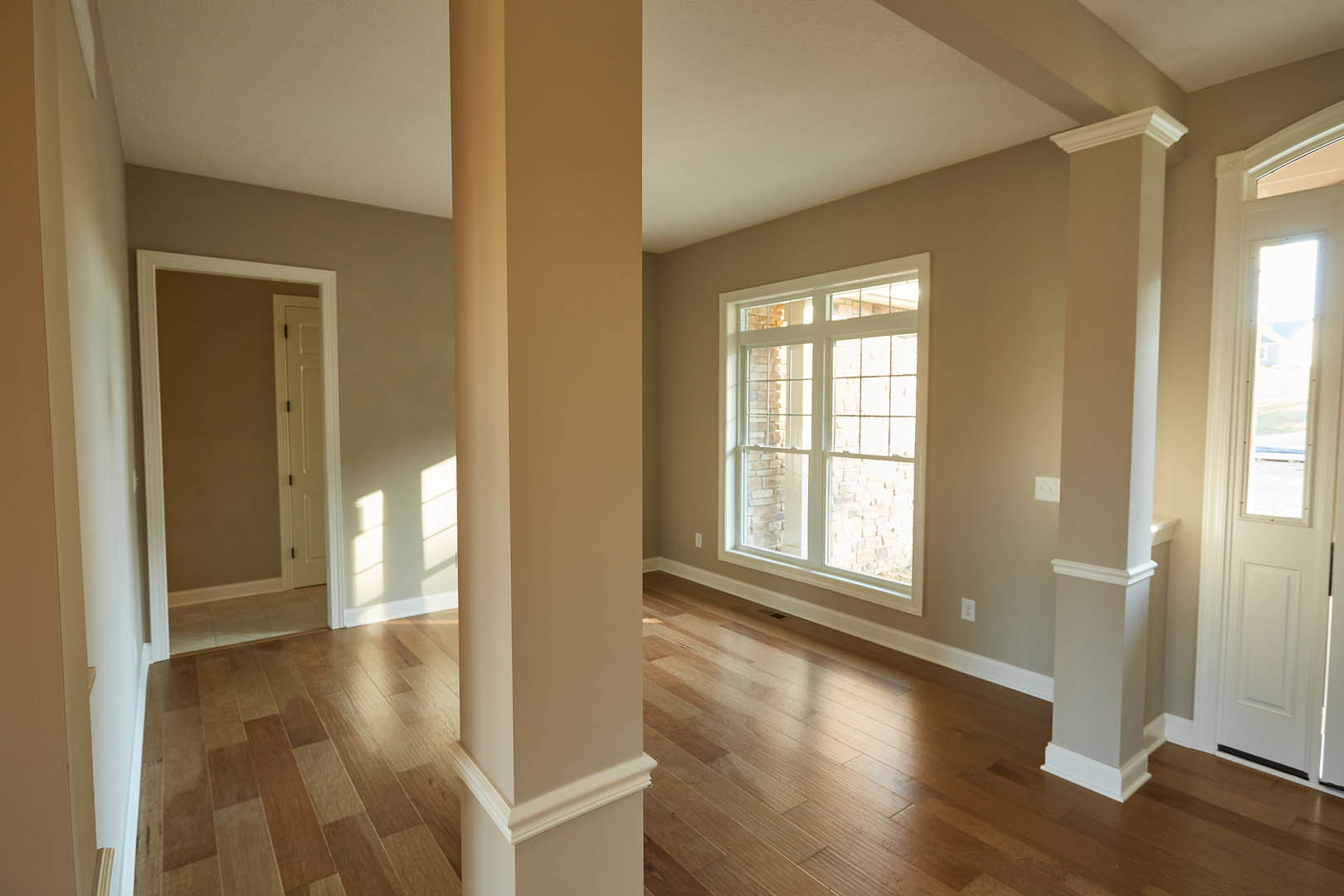 Hardwood floor with white walls, large window with white frame, simple baseboard molding, natural light illuminating the room.