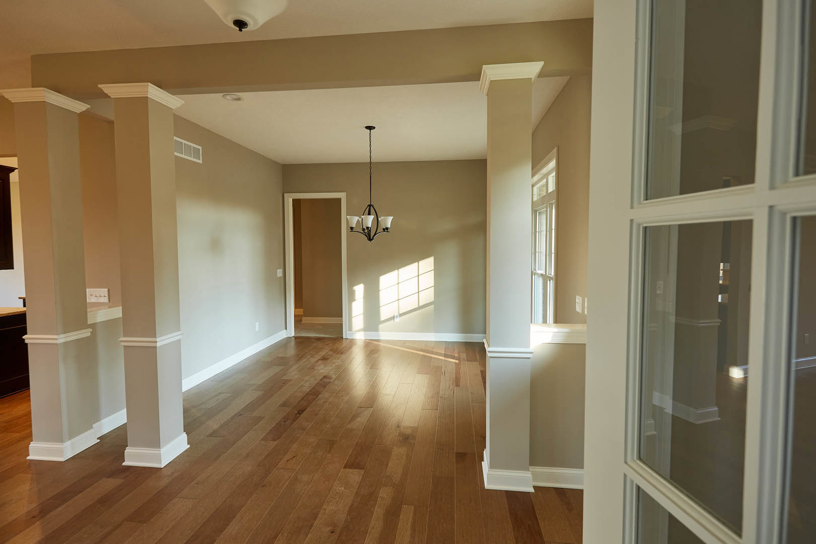 Wood floor room with white trim, brown accent wall, ceiling chandelier, and window with white frame