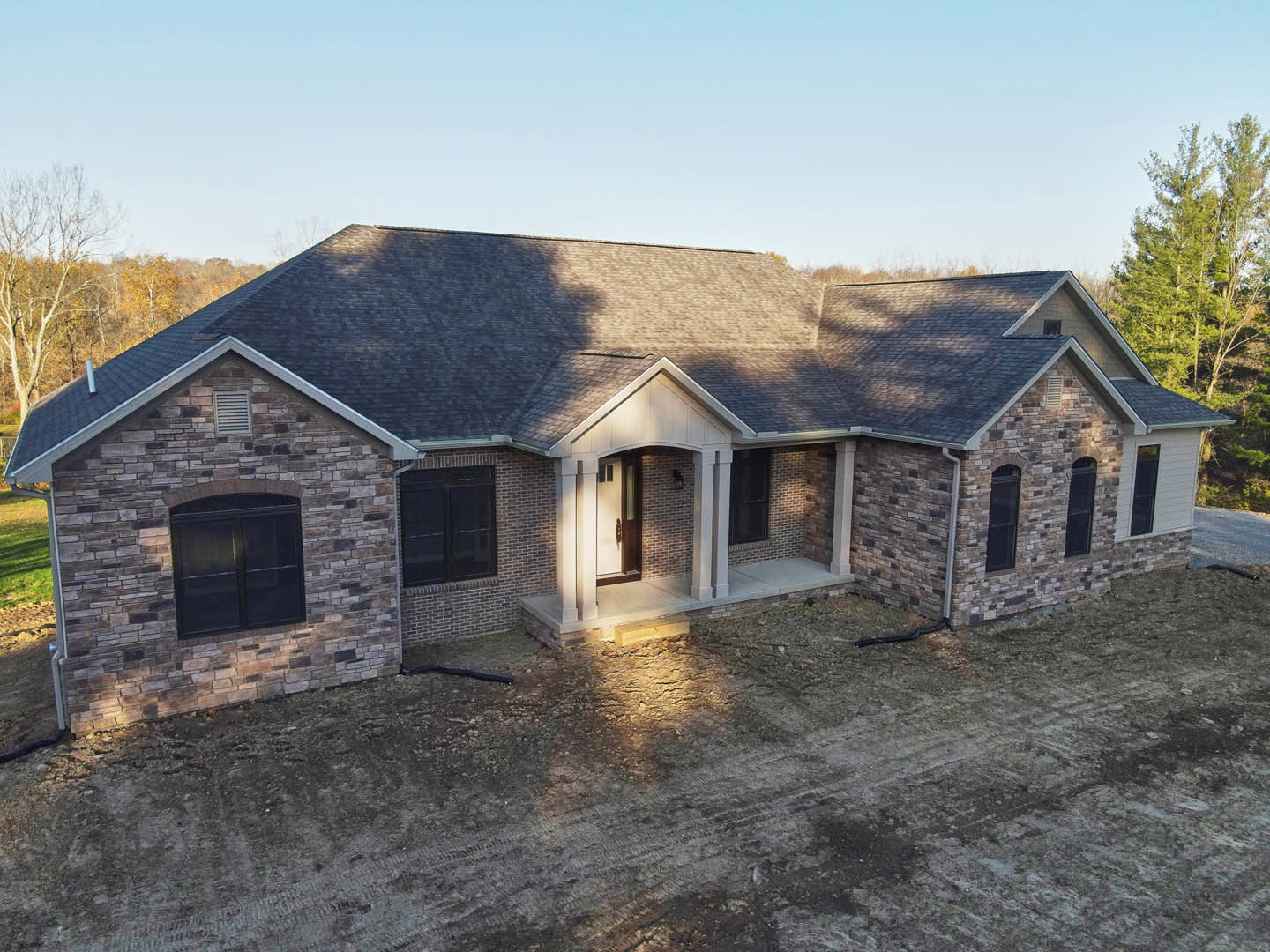 Brick and stone exterior home with black double front doors featuring glass panels, dirt landscaping area, front porch light, and blue sky overhead