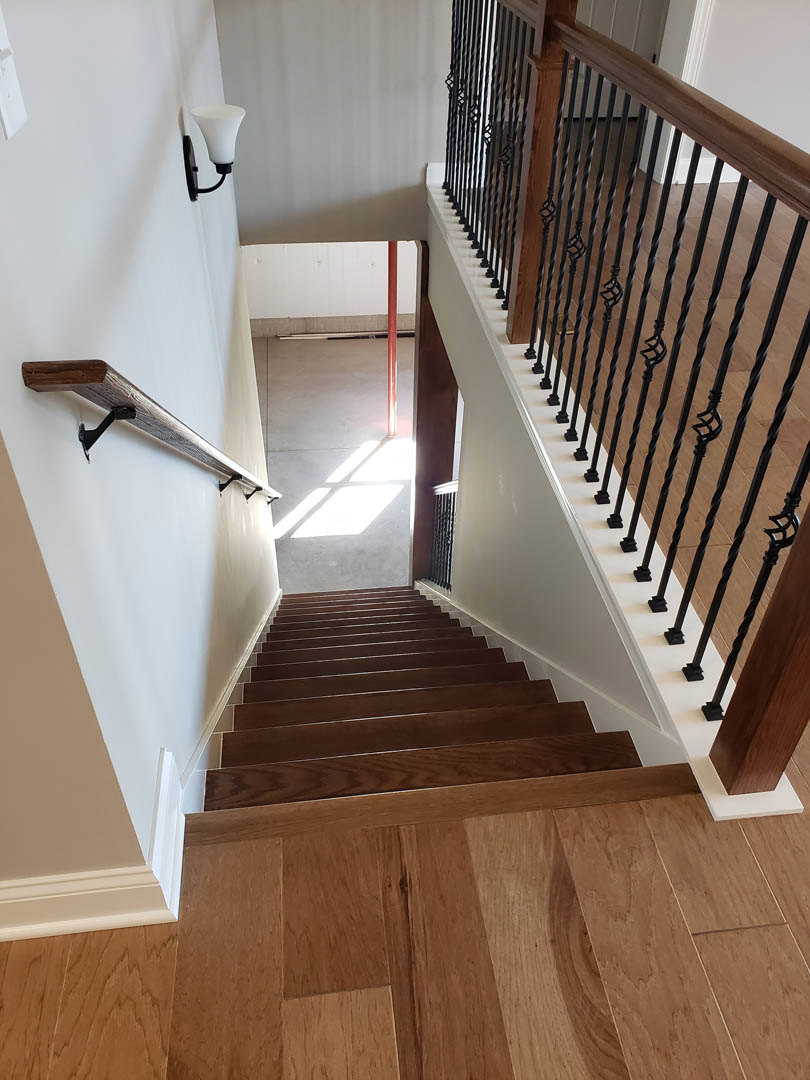 Curved wood staircase with black metal railing, light hardwood flooring, white walls, and a floor lamp with a white shade on a black pole.
