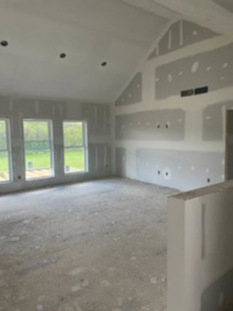 White plaster wall with black horizontal stripe, large windows overlooking green lawn, concrete flooring, and ceiling with recessed lighting.