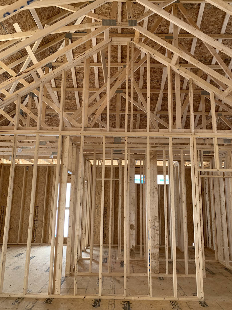 Exposed wooden roof truss and framing with partially constructed brick wall in residential home interior