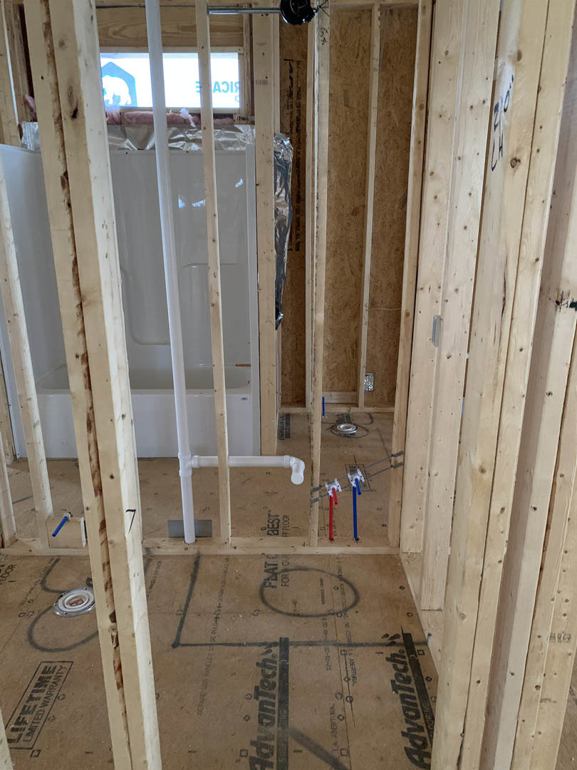 Bathroom under construction featuring exposed wood framing, unfinished walls, cardboard covering the floor, and a window letting in natural light