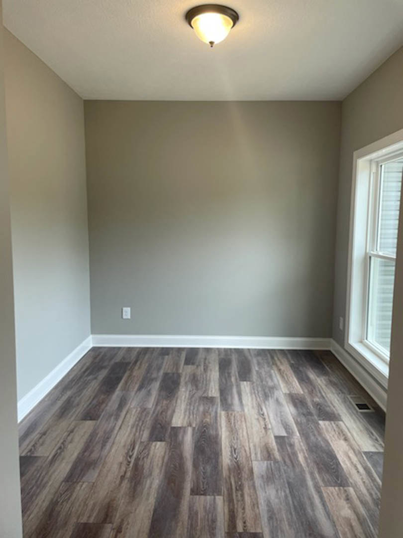 Wood floor with rectangular pattern, white trim, plaster walls, ceiling light fixture, large window letting in natural light