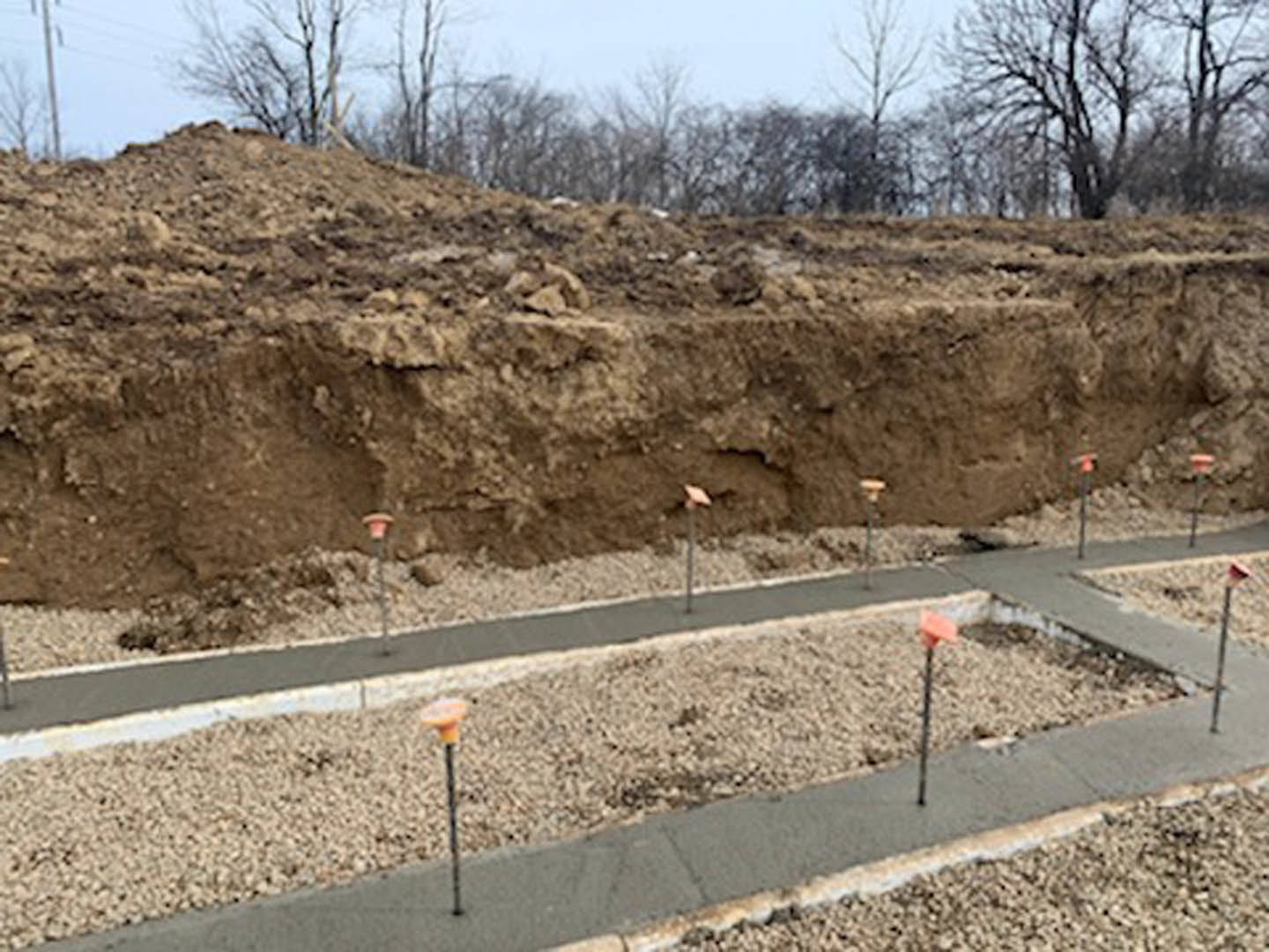 Dirt hill with a gravel path, wooden poles, and surrounding trees under a clear sky