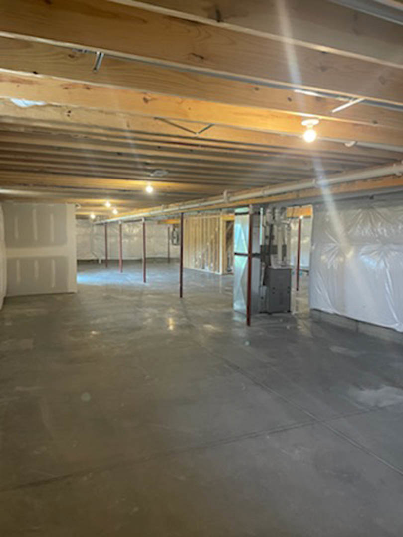 Concrete floor room with exposed ceiling beams, plaster walls, overhead light fixture, and a large metal box along one wall