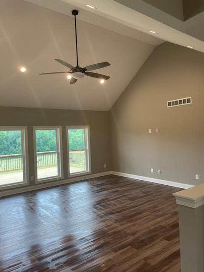 Ceiling fan with lights above wood flooring, white pillar, and row of square windows in a bright room