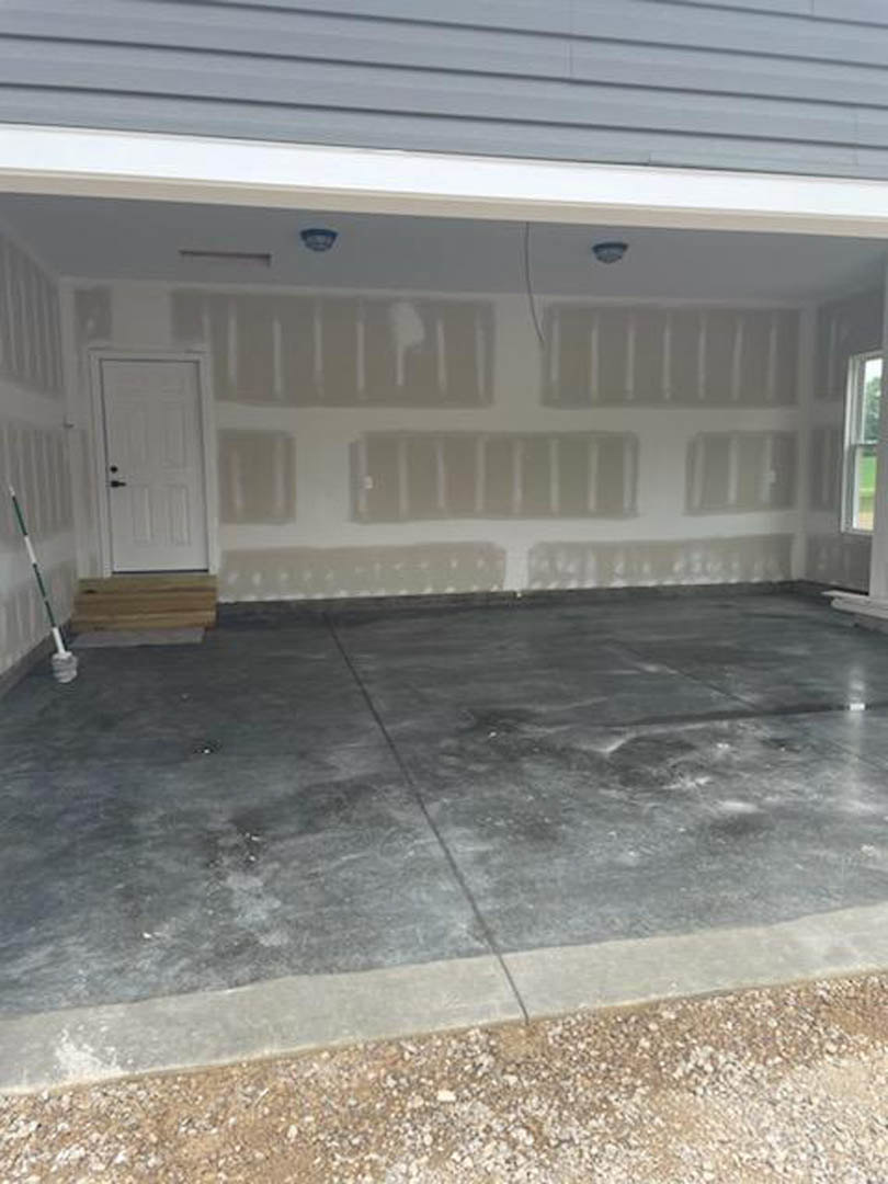 Garage exterior with white paneled door, adjacent white entry door with black handle, concrete driveway showing visible crack, green and white pole near sidewalk, wood flooring