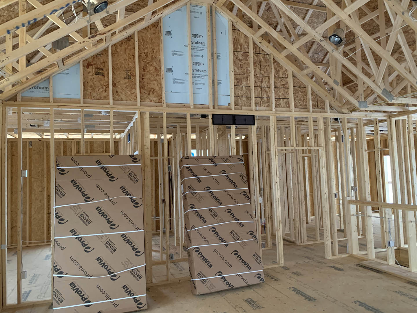 Unfinished interior with exposed wooden beams, stacked cardboard boxes, and construction materials scattered across the floor