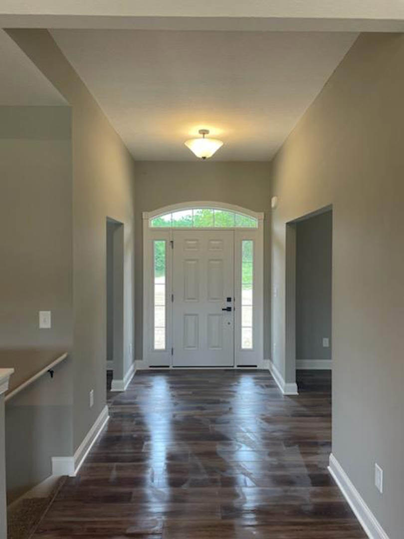 Hallway with dark wood floors, white door featuring glass panes and black handles, ceiling light fixture, white plaster walls