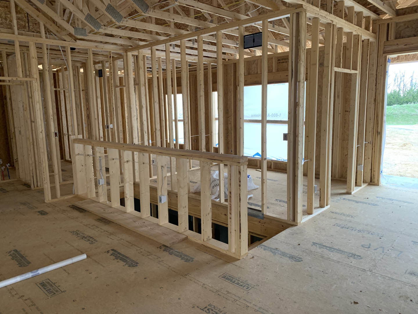 Exposed wooden beams and framing with construction materials and insulation visible on the unfinished floor inside a residential home under construction