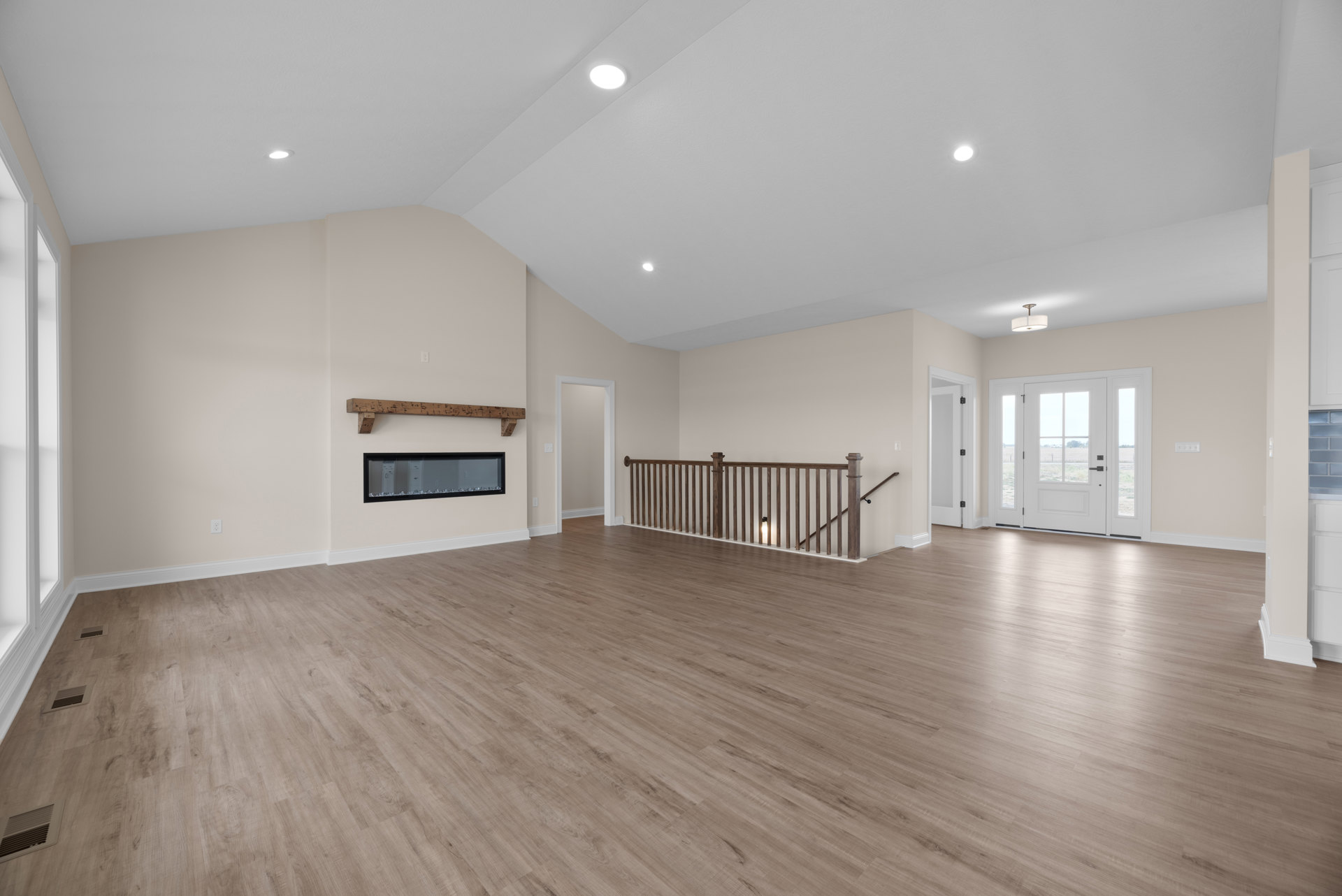 Spacious room with hardwood flooring, white walls, black-framed doorway, glass-paneled white door, staircase with metal railing, wall vent, and recessed lighting