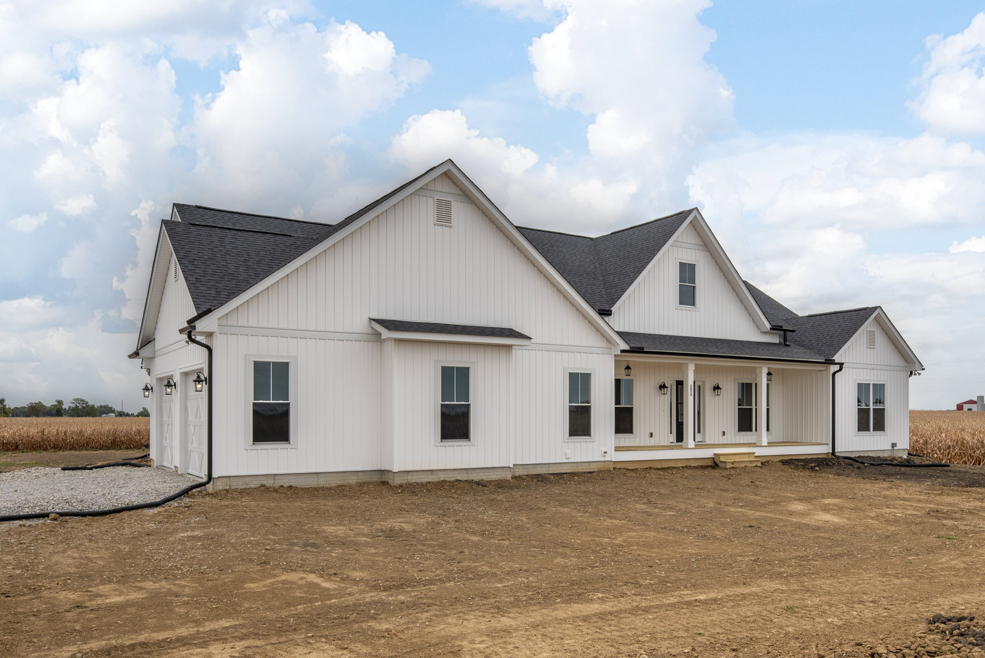White house with black roof, white-framed windows, gravel and rocks in dirt field, blue sky with clouds