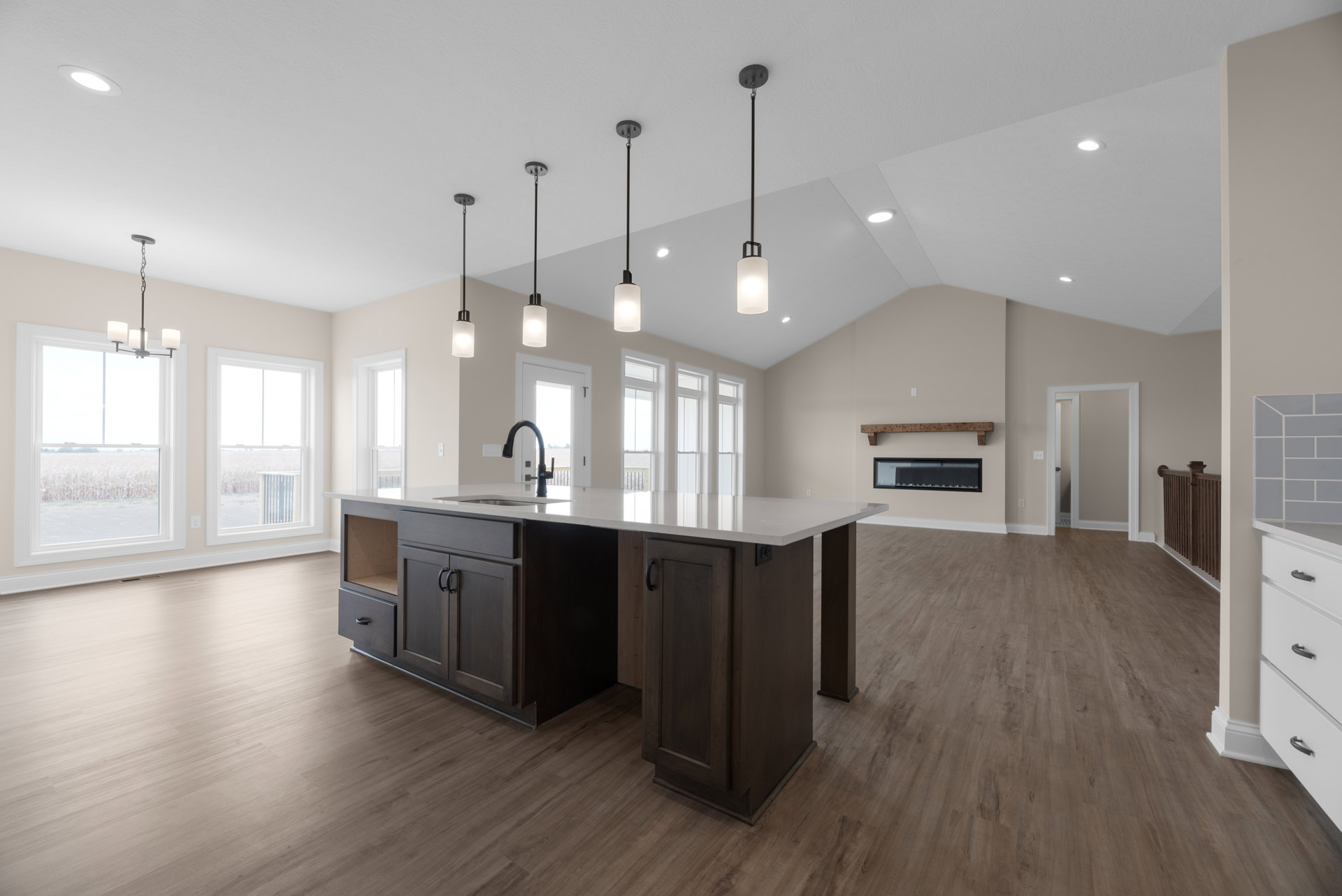 Spacious kitchen featuring a large central island with built-in sink, black faucet, white cabinetry, and drawers; wide window overlooks a cornfield, filling the room with natural