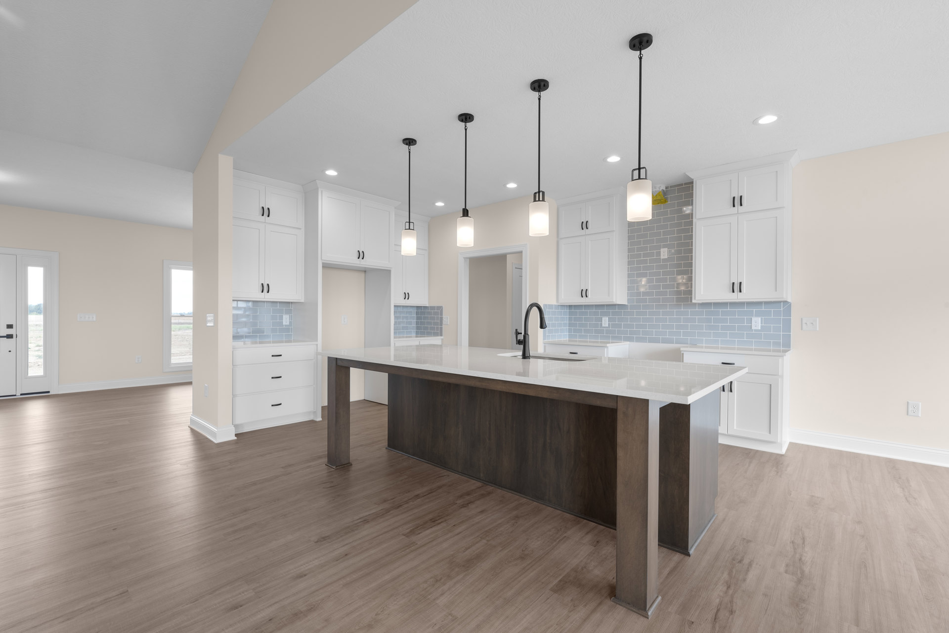 Open kitchen featuring a central island with white countertop, wood flooring, stainless steel sink and tap, white cabinetry, recessed lighting, and a white door with glass window.