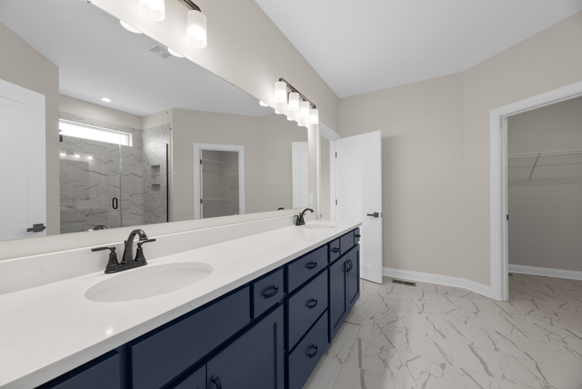 Bathroom with blue cabinets, large wall mirror, white sink, glass shower door, and built-in shelving